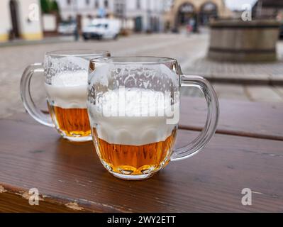 Tazze da birra o bicchieri da birra sul tavolo in legno della città sullo sfondo. Foto Stock