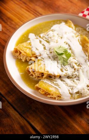 Enchiladas verdi. Tipico piatto messicano con una tortilla di mais piegata o arrotolata ripiena di pollo grattugiato e ricoperta di salsa verde piccante, cre Foto Stock