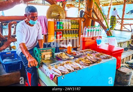 PHANG NGA, TAILANDIA - 28 APRILE 2019: Il mercante anziano gestisce una smerigliatrice di calamari secchi a manovella in una piccola bancarella di mercato a Ko Panyi galleggiante Foto Stock