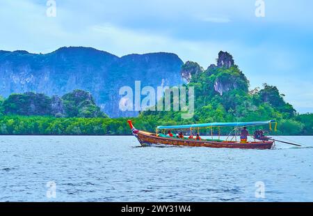 La tradizionale barca a coda lunga in legno galleggia lungo le mangrovie e le rocce, Phang Nga Bay, Thailandia Foto Stock