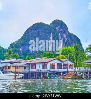 La linea di palafitte lungo la riva con alte palme e una montagna sullo sfondo, Phang Nga Bay, Thailandia Foto Stock