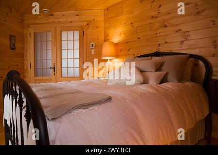 Letto queen size con copriletto bianco, getti e cuscini, testata e poggiapiedi in ghisa tubolare nella camera da letto principale con pareti in legno di pino Foto Stock