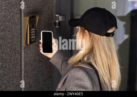 Donna che blocca lo smartlock sulla porta d'ingresso utilizzando uno smartphone. Concetto di utilizzo di serrature elettroniche intelligenti con accesso senza chiavi. Foto Stock