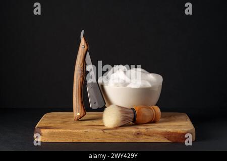 Apparecchiatura di rasatura classica con rasoio, spazzola e sapone su supporto in legno su sfondo scuro Foto Stock