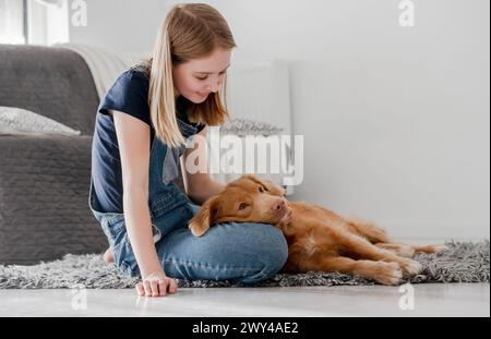 La ragazza di 11 anni gioca con Nova Scotia Retriever Toller a casa sul pavimento Foto Stock