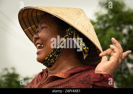 Donna contadina nel campo di riso che fa una risata... Ritratto di felice agricoltore vietnamita nella risaia. Donne che indossano un cappello vietnamita. Non la Foto Stock