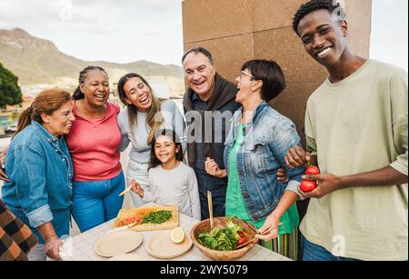 Felice famiglia multirazziale che prepara il pranzo domenicale sul tetto di casa - persone multigenerazionali che si divertono in primavera - attenzione principale sulla donna giusta f Foto Stock