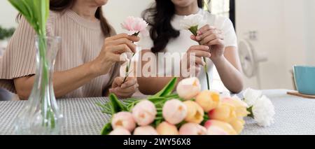 Madre anziana e figlia adulta felici sul tavolo mentre sistemano i fiori in un vaso insieme. Tecnologia e stile di vita. Buon tempo insieme Foto Stock