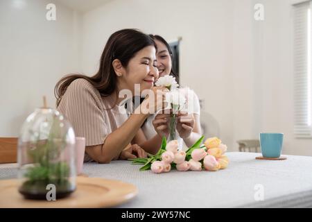 Madre anziana e figlia adulta felici sul tavolo mentre sistemano i fiori in un vaso insieme. Tecnologia e stile di vita. Buon tempo insieme Foto Stock