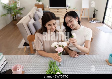 Madre anziana e figlia adulta felici sul tavolo mentre sistemano i fiori in un vaso insieme. Tecnologia e stile di vita. Buon tempo insieme Foto Stock