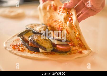 Le mani dello chef coprono gli ingredienti sull'impasto mentre preparano il tradizionale calzone italiano, la messa a fuoco selettiva e lo sfondo sfocato Foto Stock