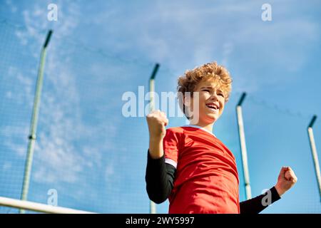 Un ragazzo con una vivace camicia rossa regge con sicurezza una mazza da baseball, pronta a dondolare. La sua espressione concentrata e la forte presa indicano il suo passaggio Foto Stock