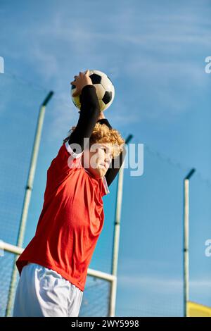 Un uomo giovane solleva con gioia un pallone da calcio nel cielo, celebrando la sua abilità atletica e il suo amore per lo sport. La sua espressione trasuda Foto Stock