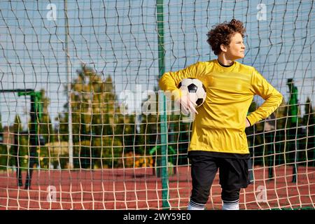 Un uomo con una camicia gialla brillante regge con sicurezza un pallone da calcio, mostrando la sua passione per questo sport. Foto Stock