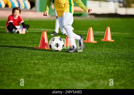 Un ragazzo determinato pratica il dribbling di un pallone da calcio intorno ai coni in un campo sportivo, mostrando la sua agilità e precisione in ogni calcio. Il vibrano Foto Stock