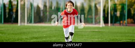 Una giovane ragazza, vestita con un'uniforme da calcio, attraversa il campo erboso con determinazione e velocità, mostrando la sua passione per lo sport. Foto Stock