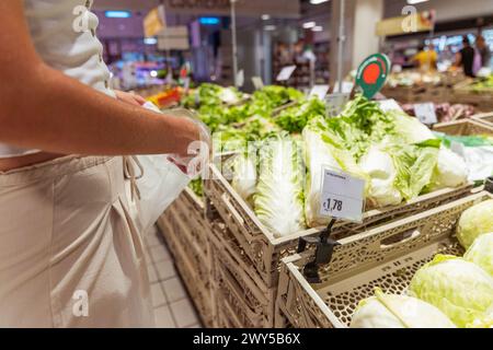 Una donna sta acquistando verdure in un negozio di alimentari. Sta guardando una mostra di lattuga e sta tenendo una borsa Foto Stock