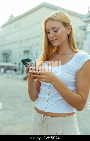 Una giovane donna usa il suo smartphone mentre è in città in estate. Foto Stock