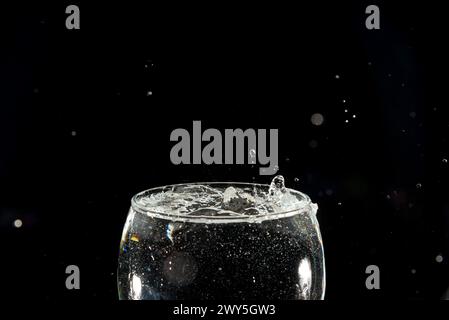 Spruzzare gocce d'acqua in un calice pieno di vetro. Effetto splash. Isolato su sfondo scuro. Foto Stock