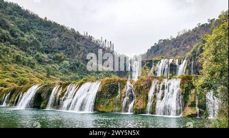 Una scenografica cascata di Jiulong che si getta in un tranquillo lago circondato da alberi in Cina Foto Stock