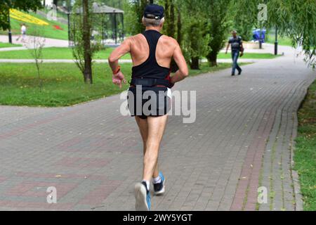 L'immagine mostra un atleta anziano vestito con uniformi sportive che corre lungo il sentiero del parco. Foto Stock