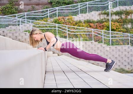 Donna fitness che fa push-up su una panchina in città. Ragazza sportiva che si allena all'aperto Foto Stock