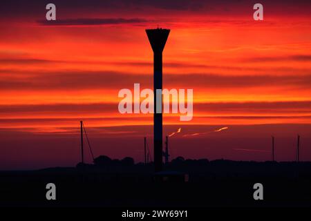 Alba sulla foce dell'Elba vicino a Otterndorf, nella bassa Sassonia. In primo piano il faro Oberfeuer Otterndorf in un cielo rosso brillante. Foto Stock