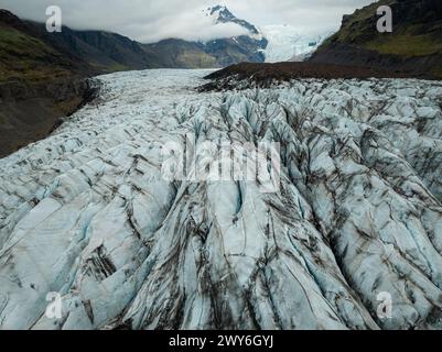 Ghiacciaio Svinafellsjokull in Islanda in una giornata nuvolosa, formazioni di ghiaccio uniche circondate da montagne, e una laguna glaciale, vista aerea. Natura e. Foto Stock