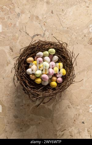 Vista dall'alto di mini uova colorate ricoperte di zucchero disposte in un nido di uccello finto. Foto Stock
