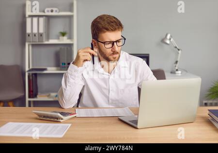 Uomo d'affari concentrato con occhiali che usa un laptop in ufficio. Foto Stock