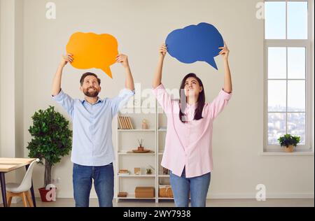 Coppia in piedi a casa con vuote e colorate bolle di discorso sopra la testa per i pensieri. Foto Stock