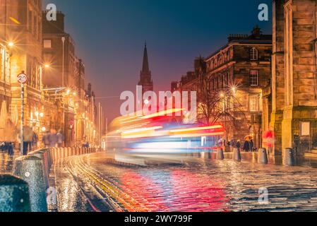 Le luci dell'auto percorrono la strada acciottolata High Street di notte lungo un tratto conosciuto come Royal Mile nella città vecchia di Edimburgo, Scozia Foto Stock