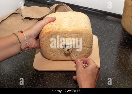 pane fatto in casa appena sfornato da una macchina per il pane. La casalinga toglie un coltello dal pane per impastare l'impasto. Foto Stock
