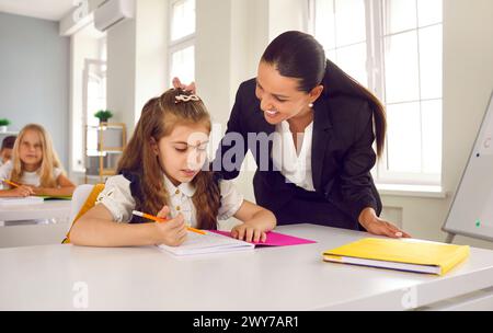 L'insegnante attento in classe durante la lezione aiuta la piccola studentessa a completare l'incarico scolastico. Foto Stock