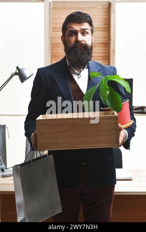 Un dipendente frustrato se ne va con una scatola dei suoi effetti personali. Essere licenziati. Bell'uomo d'affari in abbigliamento formale con scatola della sua roba. Ultimo giorno al lavoro Foto Stock