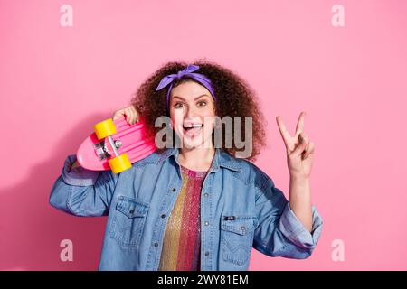 Foto di un elegante e allegro abito in denim da donna che mostra un cartello a V che regge la tavola lunga, spazio vuoto, sfondo rosa isolato Foto Stock