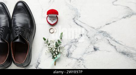 Scarpe maschili, splendidi fiori, anelli di matrimonio e fidanzamento su sfondo in marmo chiaro con spazio per il testo Foto Stock