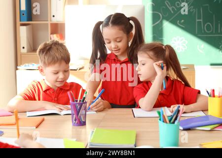 Piccoli allievi carini che scrivono a tavola in classe. Concetto di vacanze scolastiche Foto Stock