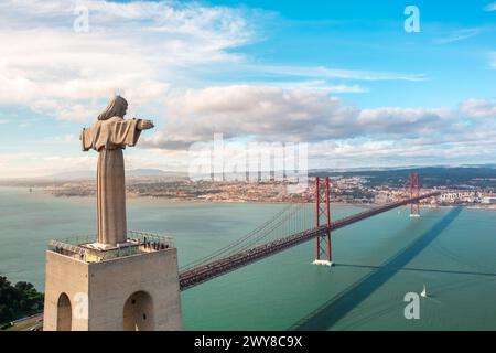 Drone che vola intorno alla gigantesca scultura Santuario del Cristo Re, affacciato sulla capitale del Portogallo Lisbona e sul Ponte de Abril 25 sul fiume Tago. Monumenti e infrastrutture a Lisbona, Portogallo Foto Stock