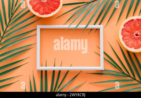 Composizione estiva creativa e alla moda composta da pompelmo e foglie di palma verde tropicale con cornice bianca su sfondo arancione. Concetto di frutta. Foto Stock