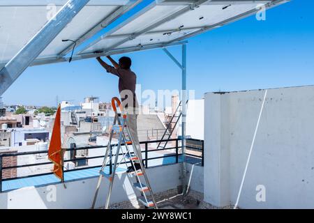 Lavoratore indiano che installa pannelli solari sul tetto della casa. Manutenzione del sistema di pannelli fotovoltaici. Concetto di energia alternativa, rinnovabile. Foto Stock