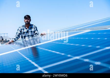 Lavoratore indiano che installa pannelli solari sul tetto della casa. Manutenzione del sistema di pannelli fotovoltaici. Concetto di energia alternativa, rinnovabile.Copia spazio Foto Stock