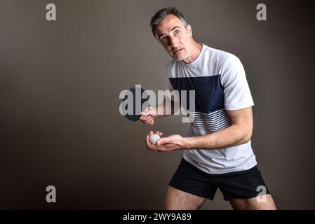 Ritratto del giocatore di ping pong pronto a servire con una palla arancione in mano su sfondo grigio isolato. Foto Stock