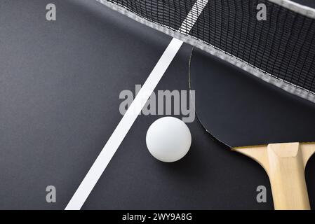 Dettaglio del paddle da ping pong con gomma nera e palla bianca sul tavolo da gioco nero. Vista dall'alto. Foto Stock