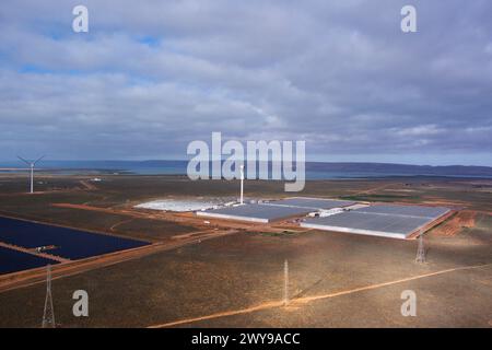 Vista aerea di turbine eoliche e pannelli solari su un paesaggio arido sotto il cielo nuvoloso con corpo d'acqua distante Foto Stock