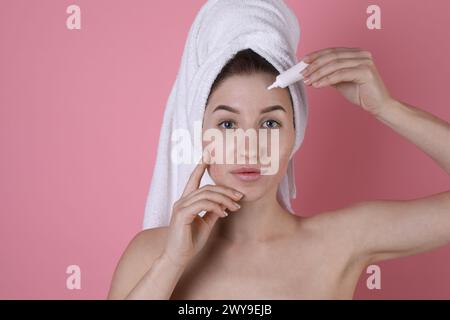 Giovane donna con problemi di acne che applica il prodotto cosmetico sulla pelle su sfondo rosa Foto Stock