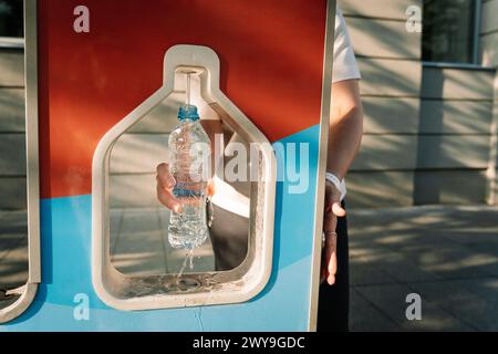 Una donna versa acqua potabile pulita in una bottiglia in una stazione di acqua potabile installata in una strada della città. Concetto di consumo sostenibile di Foto Stock