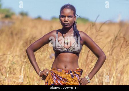 Senegal, giovane donna orgogliosa con le mani sui fianchi nel campo di miglio intorno a Djogo. Foto Stock