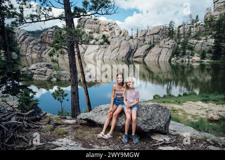 Ritratto di due ragazze sorridenti sedute sulla roccia di fronte al lago. Foto Stock
