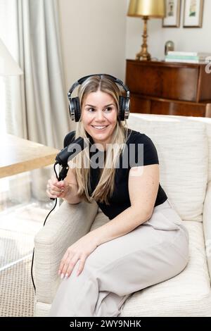 Donna allegra con microfono e cuffie in configurazione home podcast Foto Stock